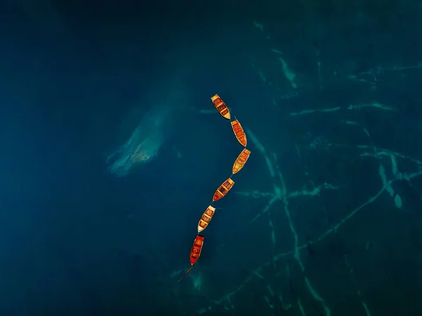 Hava görüntüsü mavi sulardaki renkli tekneleri gösteriyor. Çevresindeki doğayla uyum içindeler.