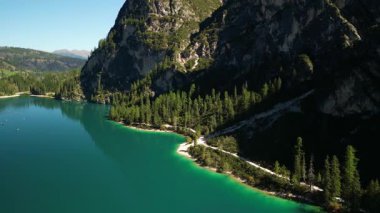 Çam ormanı, kayalık uçurumlar ve dolambaçlı bir sahil yolu ile çevrili bir turkuaz alp gölünün hava görüntüsü..