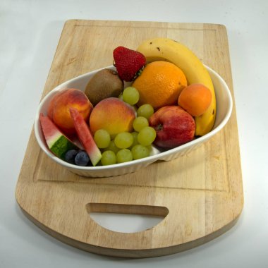 Tahta kesme tahtasındaki bir kasede renkli tropikal meyve koleksiyonu. Beyaz üzerine izole edilmiş mango çilek ve muz da dahil. Yüksek görünüm doğal meyve görüntüsü.