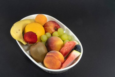 Siyah arka planda izole edilmiş mango çileği ve muz da dahil olmak üzere bir kase renkli tropikal taze meyve. Yüksek görünüm doğal meyve görüntüsü.