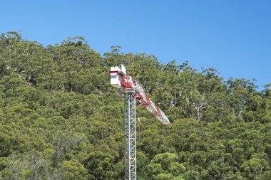 Yeşil çalı ve mavi gökyüzü arka planına sahip inşaat vinci. Gosford, NSW, Avustralya - 11 Ocak 2021: Ticari kullanım serisinin bir bölümü.