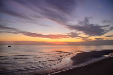 Göz kamaştırıcı, parlak, pembe ve gri sirostratus bulutlu, tropikal okyanus, güneş doğuşu deniz manzarası ve okyanus suyu yansımaları. Huay Yang, Tayland.