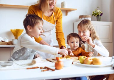 Üç çocuk, sevgi dolu bir anneyle birlikte ev mutfağında turta hazırlıyor. Aile evde yemek pişirmeyi, çocuğa öğretmenlik yapmayı, hafta sonunu birlikte geçirmeyi, yardım etmeyi, mutlu ebeveynlik kavramını sever.