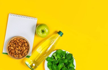 Sağlıklı yaşam tarzı konsepti, temiz su içmek, sağlıklı beslenmek. Düz badem, elma, ıspanak yaprakları, parlak sarı arka planda bir şişe su.