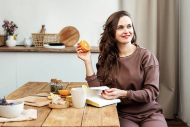 Genç bir kadın elinde portakal rengi bir kitapla mutfakta oturuyor. Enfeksiyonu önlemek için izole etti. Kız pencereden bakıyor.