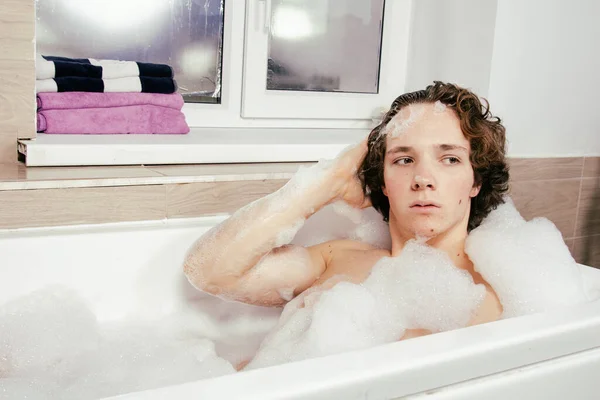 年轻迷人的小伙子躺在一个泡着泡沫的浴缸里 — 图库照片
