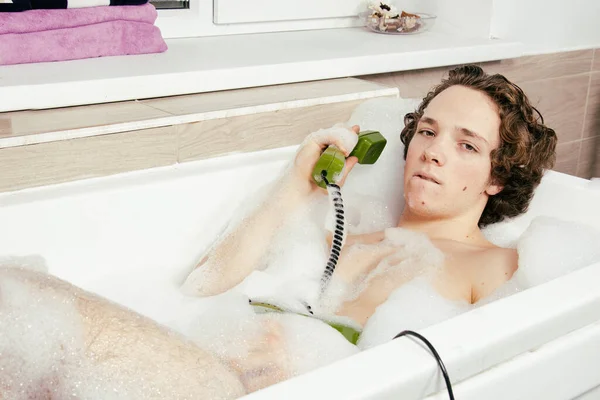 年轻迷人的小伙子躺在一个泡着泡沫的浴缸里 — 图库照片