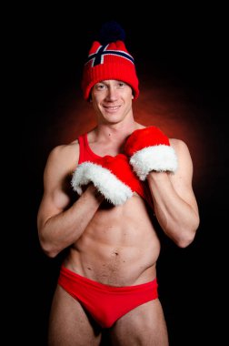 Seksi Noel Baba. Vücut geliştirici genç yakışıklı noel baba gülümsemesi takan Noel baba şapkası takan yeni yıl arifesinde ve Noel tatilinde karın kaslarını gösteriyor..
