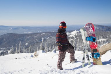 Dağın tepesinde snowboard kıyafeti giymiş bir adam. Dağların tepesinde elinde bir snowboard 'la duran genç adam.
