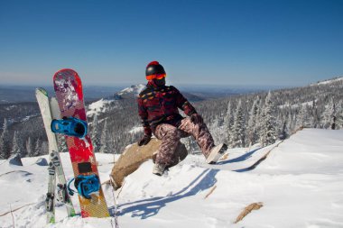 Dağın tepesinde snowboard kıyafeti giymiş bir adam. Dağların tepesinde elinde bir snowboard 'la duran genç adam.