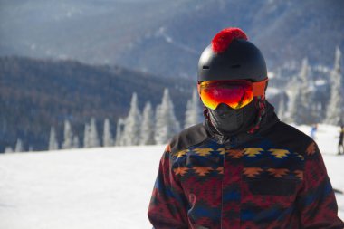 Dağın tepesinde snowboard kıyafeti giymiş bir adam. Dağların tepesinde elinde bir snowboard 'la duran genç adam.