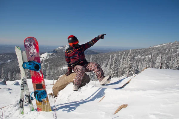 Dağın tepesinde snowboard kıyafeti giymiş bir adam. Dağların tepesinde elinde bir snowboard 'la duran genç adam.