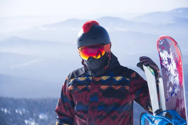 Egy férfi snowboardfelszerelésben egy hegy tetején. Fiatalember áll egy snowboarddal a hegyek tetején — Stock Fotó