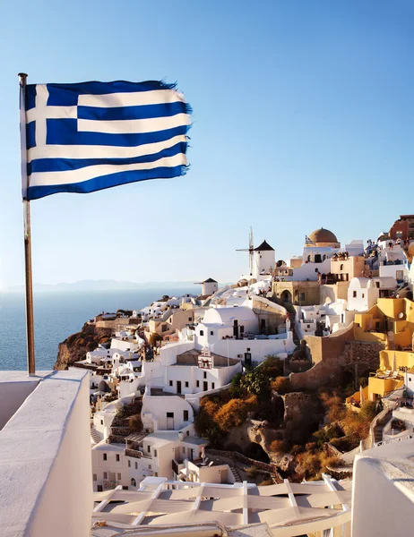 Oia, Santorini. Moinho de vento no lado do penhasco, e bandeira grega . — Fotografia de Stock