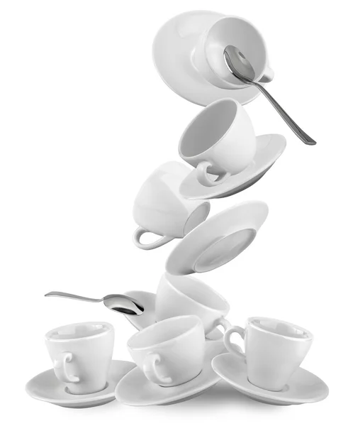 Tazze cadenti e piattini con cucchiai isolati su bianco Fotografia Stock