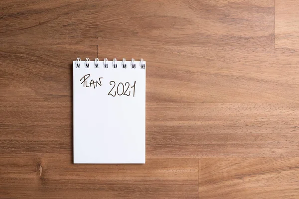 Minimalist image of a notebook to write the plan for the new year, the goals for 2021, wood table background, copy space.