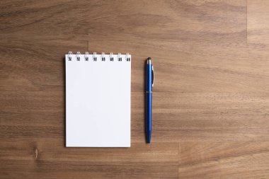 Boş bir sayfada, mavi bir kalemin yanında, ahşap bir masanın üzerinde, sarmal bir defterin modern ve basit görüntüsü. Üst görünüm, alanı kopyala.