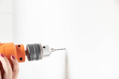 Beyaz duvarı delen matkaplı bir kadın. Resmi kopyalama alanı ile detaylandır.