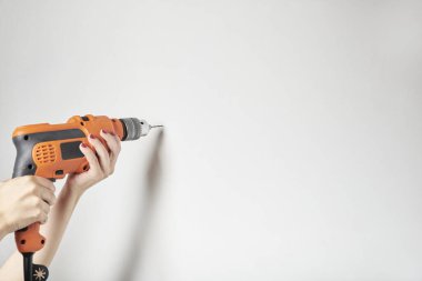 Woman with manicured hands drilling a white wall with an orange power drill. Detail image with copy space. clipart