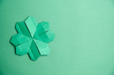 Origami yeşil arka planda yeşil kağıttan yapılmış dört yapraklı yonca. Şans ve Aziz Patrick Günü kavramları. Kopyalama alanı olan resim.