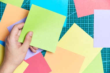 Genç bir kadın eli, diğer renkli kağıtlar ve bir paspas üzerinde boş yeşil bir kağıt tutuyor. Notlar yazmak ya da origami yapmak için gerekli malzemeler. Kopyalama alanı olan düz resim.