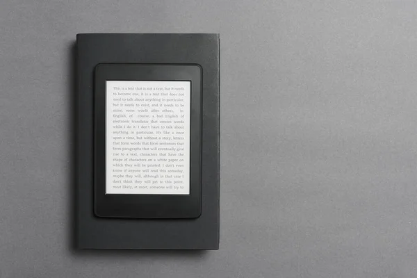 Electronic reader with text on the screen over a closed black traditional book, on a gray background. Concepts of technology, modernity and reading. Flat lay image with copy space.