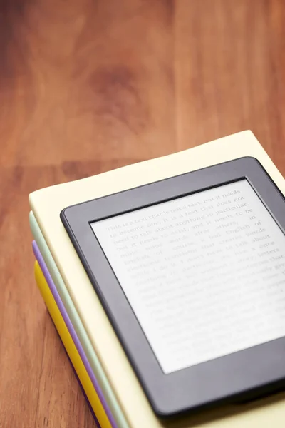 Electronic reader with a text on the screen on a stack of books on a wooden desk. Concepts of technology, reading and education.