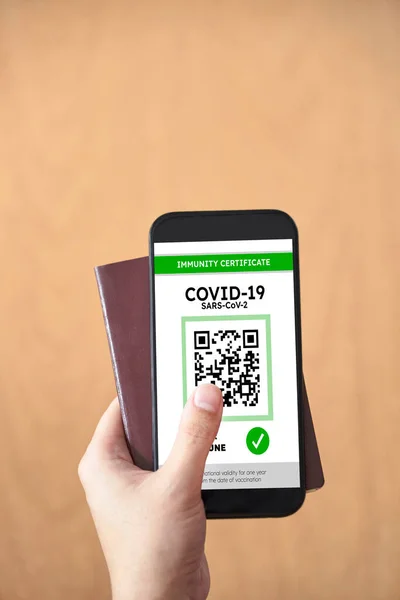Hand holding a passport and a smartphone with a Covid19 immunity certificate on the screen. Concept of travel during the Corona virus pandemic. Image with copy space.