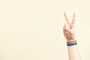 Genç el zafer ya da barış işareti yapıyor, gökkuşağı bileziği takıyor, LGBT sembolü. Mücadele kavramları, eşcinsellerin gücü ve gururu, lezbiyenler, biseksüeller ve transseksüeller. Kopyalama alanı olan resim.