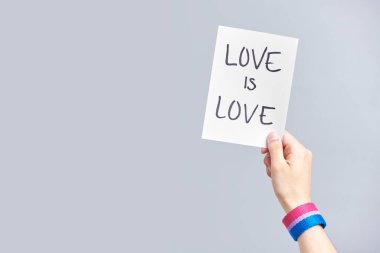 Elinde biseksüel bayrak bileziği olan genç bir el yazısı olan bir kağıt parçası: Aşk aşktır. Aşk kavramları, cinsel çeşitlilik ve ayrımcılık karşıtlığı. Kopyalama alanı olan resim.