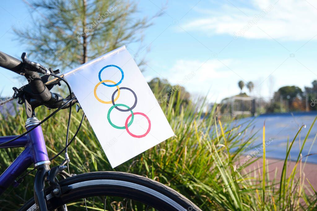 Homemade olympic flag made of paper put on the front of a bicycle, outdoors, in a sports environment, a sunny day. Image with copy space.