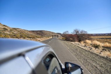 Arabayla seyahat etmek: ön planda, bir aracın yanında; arka planda, Loncopue, Neuquen, Arjantin girişini gösteren kemere giden yol..