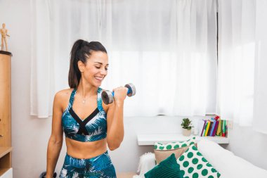 Oturma odasında ağırlık kaldıran mutlu genç bir kadın.