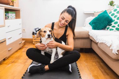 Genç bir kadın köpeğiyle evde egzersiz yapıyor.