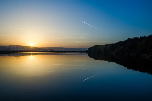 Lake sunset view with jet plane trail — Stock Photo, Image