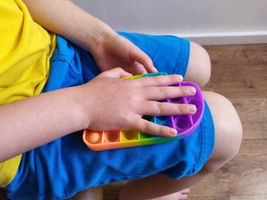 Mavi şortlu çocuk renkli poppit oyuncağıyla oynuyor. Çocuklar ve yetişkinler için stres önleyici oyuncaklar