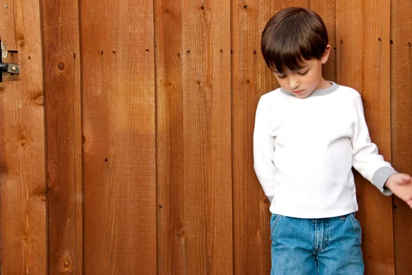 Young boy looking down on wood fence — Stock Photo, Image