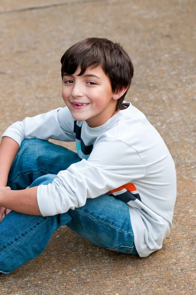 Cute young boy sitting on sidewalk looking at camera — Stock Photo, Image