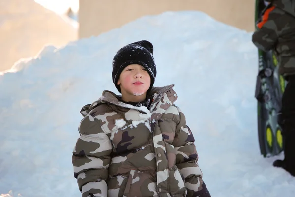 Lindo niño en camuflaje esquí chaqueta comer nieve . —  Fotos de Stock