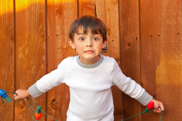 Adorable little boy holding Christmas lights looking surprised. — Stock Photo, Image