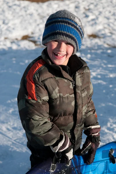 Adorable niño sosteniendo trineo sonriendo a la cámara usando camuflaje — Foto de Stock