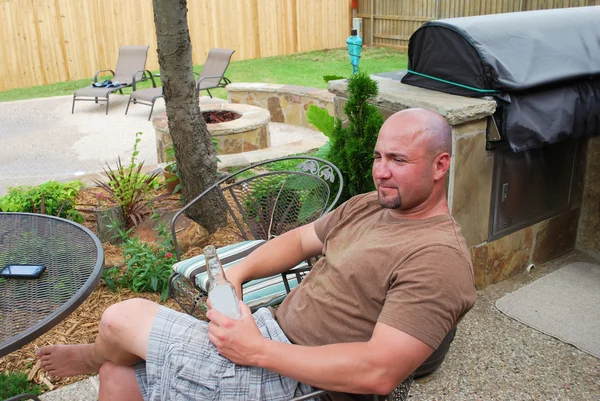 Handsome bald man drinking beer in backyard patio. — Stock Photo, Image