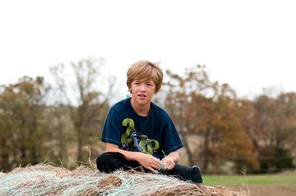 Młody chłopak siedzący na belę siana — Zdjęcie stockowe