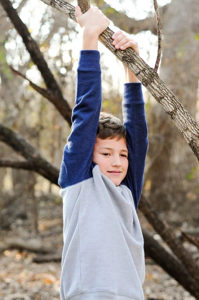 Roztomilý malý kluk visí z větve stromu. — Stock fotografie