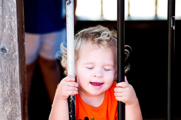 Adorable little toddler girl in pumpkin shirt behind bars. — Stock Photo, Image