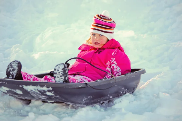 Süße blauäugige Mädchen auf einem Schlitten im Schnee. — Stockfoto