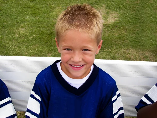 Roztomilý malý chlapec seděl na lavičce fotbalové hry. — Stock fotografie