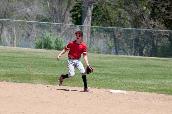 Teenage baseball shortstop körs på fältet. — Stockfoto