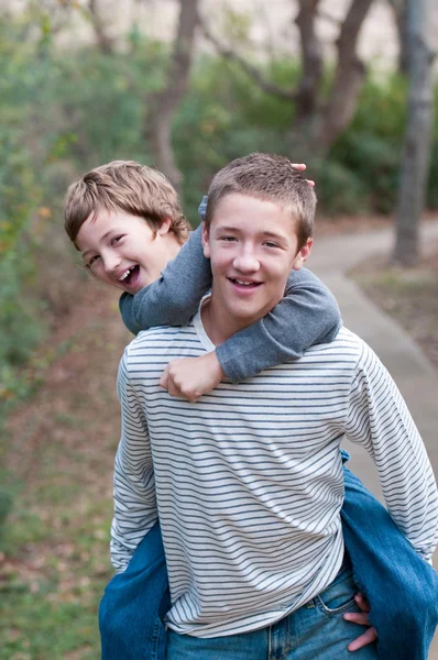 Happy brothers riding piggyback at the park — Stock Photo, Image