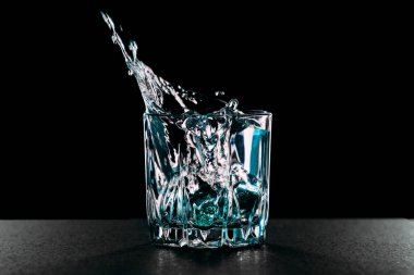 Cinle bardağa buz düşmesi. Siyah arka planda alkollü cam. Sıvı damlaları.